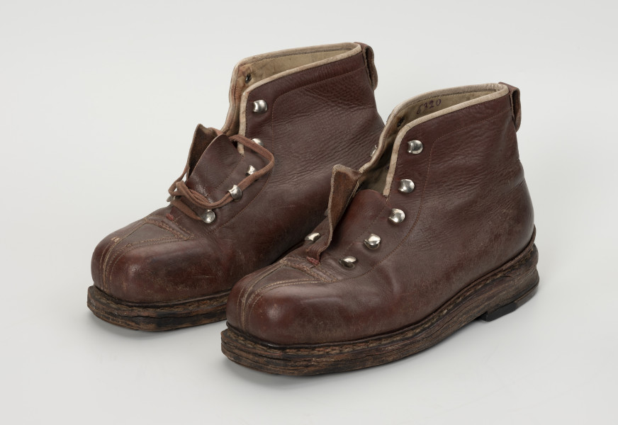 para trzewików - Ujęcie ze skosu z prawej; Para damskich, brązowych, sznurowanych butów. Otwory na sznurówki zabezpieczone metalowymi obwódkami. Cholewka wykonana ze skóry licowej bydlęcej. To naturalna skóra, której zewnętrzna warstwa została poddana obróbce mechanicznej powodującej jej gładką fakturę. Między płaty skóry wszyte skórzane wzmocnienia na noski. Podeszwy złożone z kilku warstw kruponu (najgrubszej części surowej skóry bydlęcej). Podeszwa zszywana. W wyniku zużycia skóry dosztukowane w latach późniejszych nowe warstwy kruponu z przodu podeszwy oraz fleki wykonane z gumy obuwniczej. Buty noszą ślady dużej eksploatacji, uszkodzenia skóry przy górnym zakończeniu buta oraz po całości widoczna popękana skóra.