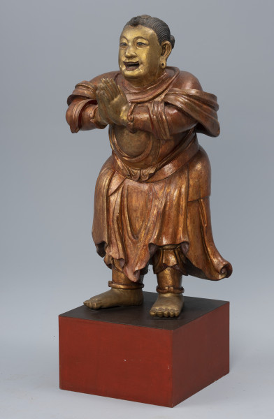 pielgrzym Shancai Tongzi (?) wraz z wypełnieniem - ujęcie z przodu z prawej; Monumentalna, drewniana, złocona rzeźba postaci męskiej w pozie adoracji przedstawia prawdopodobnie młodego pielgrzyma. Postać stoi na postumencie z rękami wyciągniętymi przed siebie i dłońmi złożonymi w pełnym szacunku geście. Ma pogodny wyraz twarzy, lekko uniesione brwi, duże, brązowe oczy, podłużne uszy i otwarte, lekko uśmiechnięte usta z widocznym uzębieniem. W jego policzkach zaznaczono dołki, natomiast w płatkach usznych wydrążono niewielkie otwory. Gładko zaczesane czarne włosy zwijają się w niewielkie koczki: z przodu jeden i z tyłu dwa. Pielgrzym ubrany jest w długie, kilkowarstwowe, sięgające za kolana szaty, natomiast z jego ramion i rąk opada tkanina w formie szala. Na jego obu nadgarstkach i kostkach widoczne są bransolety. Stopy ma nagie.