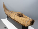 caballito de totora (łódź trzcinowa) - Ujęcie z prawej; Ponad czterometrowa łódź trzcinowa o naturalnym jasnobrązowym kolorze z wysoko zadartym ku górze długim, zwężającym się dziobem z tyłu oraz grubą, płasko ściętą rufą z przodu. Kształtem przypomina gruby cios słonia. Została zbudowana z dwóch wiązek trzciny mocno skrępowanych przez poprzeczne wiązania. W ten sposób nadano łodzi pożądany, żeglowny kształt. Wśród wiązek trzcinowych tworzących rufę uformowano trójkątne zagłębienie służące do przechowywania narzędzi rybackich (sieci, lin, pułapek) i złowionych zdobyczy.