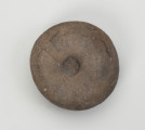 kamień kanelowany (kamień żłobkowany) - Ujęcie z góry; Narzędzie kamienne z szarobrązowego otoczaka, widoczne koliste wgłębienie. Powierzchnia dość gładka, ślady obróbki widoczne na całej powierzchni.