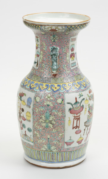 wazon typu famille rose - ujęcie z drugiego boku; Porcelanowy wazon zdobiony wielobarwną dekoracją naszkliwną w pastelowych odcieniach z przewagą różu w typie famille rose. Kształt gruszkowaty, szyja szeroka zakończona rozszerzającym się wylewem. Wazon bogato zdobiony licznymi motywami dekoracyjnymi. W jego górnej części z przodu widoczny uchwyt w kolorze pastelowej zieleni. Brzeg wylewu zdobiony dookolnie i naprzemiennie motywami stylizowanego lotosu o czerwonym kwiecie, żółtych i zielonych liściach na białym tle oraz zgeometryzowanym wzorem roślinnym w kolorach zielonym i różowym na żółtym tle. Szyję oddzielono od brzuśca biegnącymi dookolnie wzorami: ornamentem meandrycznym o różowej, żółtej i seledynowej barwie oraz znajdującym się pod nim motywem grzyba nieśmiertelności w niebieskim, żółtym, czerwonym i seledynowym kolorze. Brzusiec oraz szyję zdobią czworoboczne pola (rezerwy) o seledynowych bordiurach wypełnione tzw. motywem Stu Antyków (Hundred Antiques/Hundred Treasures) na białym tle. Ułożono je naprzeciwlegle: dwa na szyi oraz dwa na brzuścu. Pola wypełniają przedmioty i rośliny w dość nieformalnym układzie. Na brzuścu pokazano: różnorodne wazy, naczynie na wysokim stojaku oraz inne niezidentyfikowane przedmioty i rośliny. Tło stanowi przedstawiony na różowym tle motyw stylizowanego lotosu z wijącymi się liśćmi. Dół wazonu ozdobiony dookolnie geometrycznym motywem w postaci pionowych żółtych i różowych pasków na seledynowym tle.