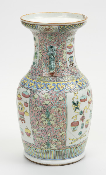 wazon typu famille rose - ujęcie z boku; Porcelanowy wazon zdobiony wielobarwną dekoracją naszkliwną w pastelowych odcieniach z przewagą różu w typie famille rose. Kształt gruszkowaty, szyja szeroka zakończona rozszerzającym się wylewem, w którym widoczny jest półokrągły ubytek. Wazon bogato zdobiony licznymi motywami dekoracyjnymi. W jego górnej części z przodu widoczny uchwyt w kolorze pastelowej zieleni. Brzeg wylewu zdobiony dookolnie i naprzemiennie motywami stylizowanego lotosu o czerwonym kwiecie, żółtych i zielonych liściach na białym tle oraz zgeometryzowanym wzorem roślinnym w kolorach zielonym i różowym na żółtym tle. Szyję oddzielono od brzuśca biegnącymi dookolnie wzorami: ornamentem meandrycznym o różowej, żółtej i seledynowej barwie oraz znajdującym się pod nim motywem grzyba nieśmiertelności w niebieskim, żółtym, czerwonym i seledynowym kolorze. Brzusiec oraz szyję zdobią czworoboczne pola (rezerwy) o seledynowych bordiurach wypełnione tzw. motywem Stu Antyków (Hundred Antiques/Hundred Treasures) na białym tle. Ułożono je naprzeciwlegle: dwa na szyi oraz dwa na brzuścu. Pola wypełniają przedmioty i rośliny w dość nieformalnym układzie. Tło stanowi przedstawiony na różowym tle motyw stylizowanego lotosu z wijącymi się liśćmi. Dół wazonu ozdobiony dookolnie geometrycznym motywem w postaci pionowych żółtych i różowych pasków na seledynowym tle.