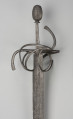 rapier - Ujęcie 3/4; Rapier o głowni prostej, obusiecznej, z ricassem. Na ricassie i krótkim odcinku głowni biegnie zaznaczone dwoma korytkami zbrocze. Rękojeść ma krzyżowy jelec w esowatej formie i rozbudowany kosz do ochrony dłoni. Kosz składa się z trzech obłęków bocznych rozchodzących się ku ostrzu i osłaniających ricasso, po drugiej stronie są dwa obłęki boczne, z których górny jest większy, połączonych „oślą podkową” i dodatkowo dwoma obłękami. Głowica jest owalna, wydłużona z wyodrębnioną podstawą w formie pierścieni, ozdobiona jest wzdłużnie nacięciami i zakuta od góry.