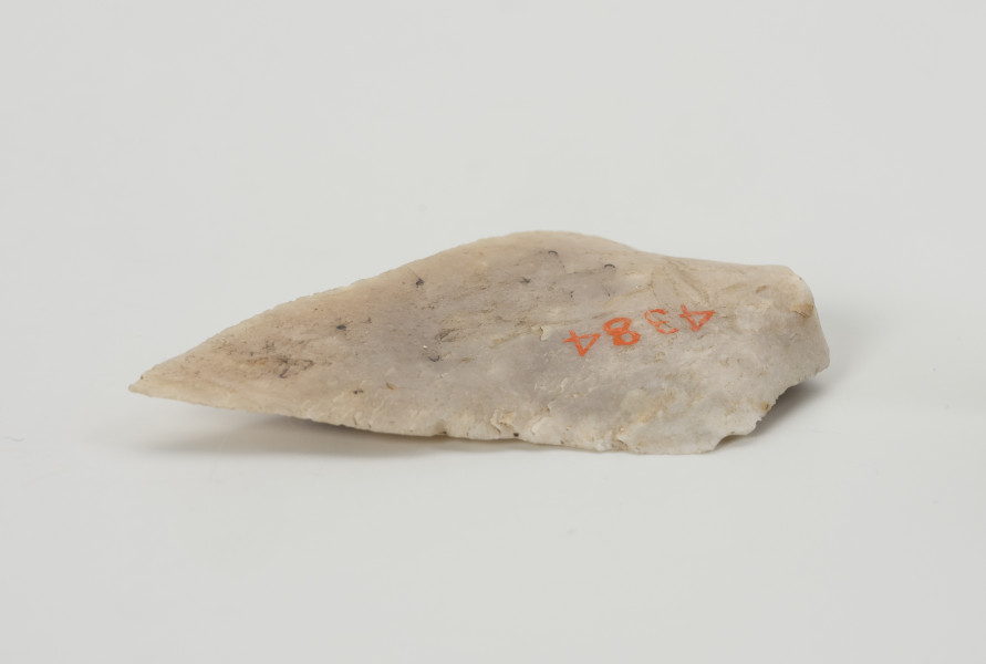 półwytwór liściaka - Ujęcie z boku; Krótki wiór w kształcie wydłużonego trójkąta, odbity miękkim tłukiem (prawdopodobnie z poroża) od większej bryły. Jego cechą charakterystyczną jest układ negatywów na stronie wierzchniej wskazujący, że zasadniczy kształt został uformowany jeszcze przed odbiciem. Jest to tzw. debitaż predefiniowany. Brakuje retuszu, który formowałby krótki trzonek. Ze względu na jego rozmiary prawdopodobnie miał służyć jako grot włóczni.