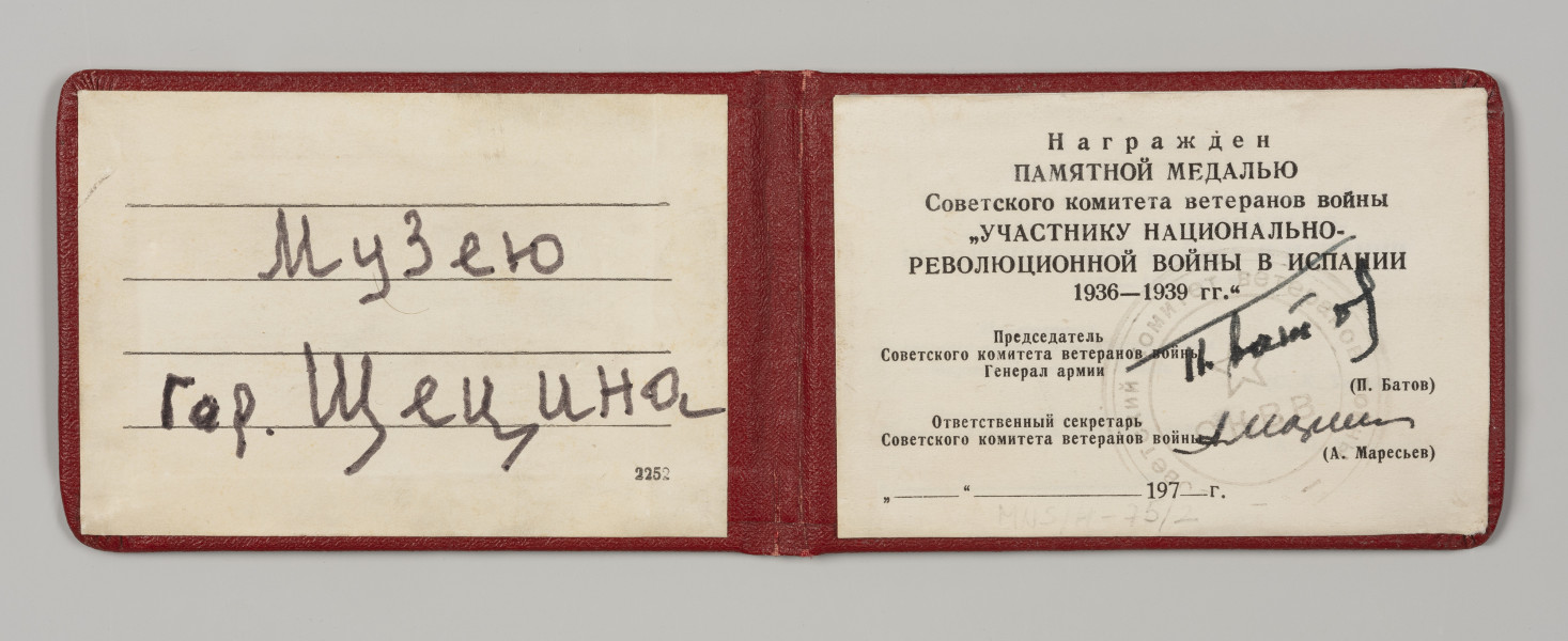 legitymacja do medalu - Ujęcie wewnątrz; Legitymacja ma formę prostokątnego dokumentu, składającego się z dwóch skrzydeł. Okładka w intensywnym odcieniu czerwieni. Na wewnętrznej stronie lewego skrzydła legitymacji widnieje dwuwierszowa, wykonany odręcznie dedykacja dla Muzeum. Na prawym skrzydle wewnętrznej strony umieszczone są drukowane informacje organu wydającego legitymację, wraz z odręcznymi podpisami władz tegoż organu.