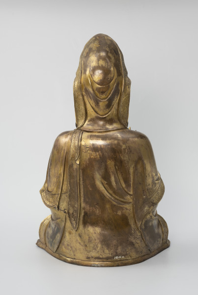 Bodhisattwa Guanyin - ujęcie z tyłu; Duża, wykonana ze złoconego brązu figura siedzącą w pozie medytacyjnej. Postać ma zaciągniętą na głowę tkaniną. Ubrana jest w długie, warstwowe, jedwabne szaty królewskie. Z tyłu figury, przy dolnej krawędzi biały napis pod postacią numeru: 1011z, natomiast w górnej części zamazany, czarny napis/znak.