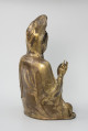 Bodhisattwa Guanyin - ujęcie tyłu ze skosu z prawej; Duża, wykonana ze złoconego brązu figura przedstawia siedzącą w pozie medytacyjnej kobietę Bodhisattwę Guanyin (chin. 观音, sanskr. Awalokiteśwara, tyb. Czenrezig). Postać ma spuszczone, przymknięte oczy, symetryczną, pełną twarz o pogodnym i spokojnym wyrazie oraz gładko zaczesane włosy, schowane pod diademem i zaciągniętą na głowę tkaniną. Ubrana jest w długie, warstwowe, jedwabne szaty królewskie. Jej prawa dłoń uniesiona na wysokości klatki piersiowej ułożona jest pionowo, jej środkowy palec i kciuk tworzą okrąg. Z tyłu figury, przy dolnej krawędzi biały napis pod postacią numeru: 1011z.