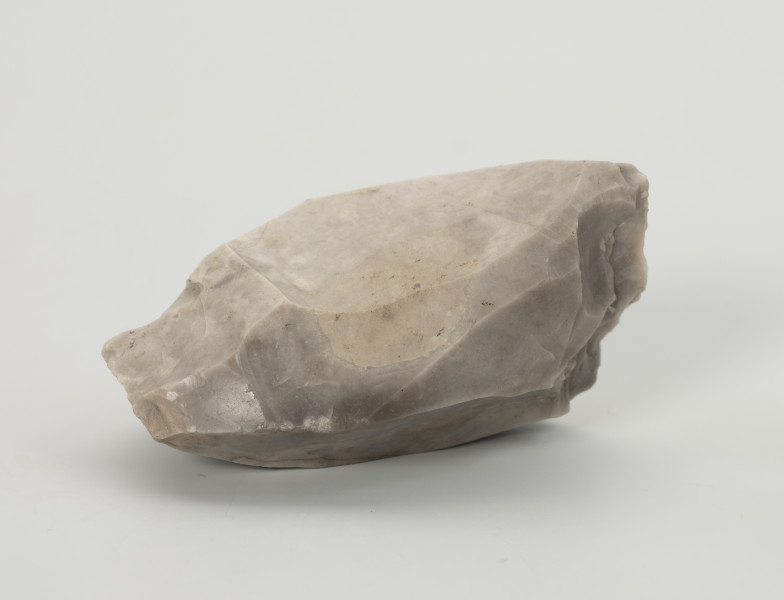 rdzeń wielopiętowy - Ujęcie z przodu; Rdzeń wielopiętowy w formie wydłużonego klina z widocznymi kilkoma miejscami, z których odbijano wióry. Strategia redukcji typowa dla rdzeni w ostatnim stadium użytkowania, szczególnie na stanowiskach bez źródeł surowca dobrej jakości w pobliżu. Ślady eksploatacji miękkim tłukiem. Bryła jasnoszarego krzemienia kredowego bardzo dobrej jakości.