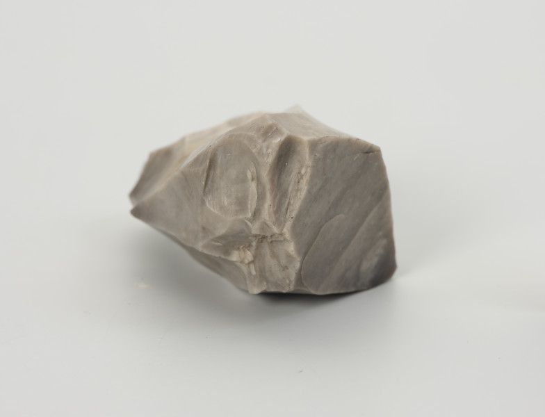 rdzeń wielopiętowy - Ujęcie z drugiego boku; Rdzeń wielopiętowy w formie wydłużonego klina z widocznymi kilkoma miejscami, z których odbijano wióry. Strategia redukcji typowa dla rdzeni w ostatnim stadium użytkowania, szczególnie na stanowiskach bez źródeł surowca dobrej jakości w pobliżu. Ślady eksploatacji miękkim tłukiem. Bryła jasnoszarego krzemienia kredowego bardzo dobrej jakości.