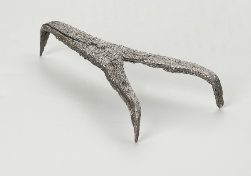 rak żelazny - Ujęcie przodu ze skosu z lewej; Rak żelazny trójramienny z czworobocznej sztabki żelaznej z haczykiem na końcu każdego ramienia.