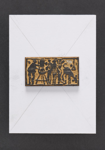 klocek drzeworytniczy - Klocek drewniany, z wyrytym tłem tworzącym wypukłą powierzchnie odbicia matrycy przedstawiającą malarza przy sztaludze po prawej stronie, dwie postacie oraz zwierzę po stronie lewej klocka drzeworytniczego. Matryca przymocowana do prostokątnego kawałka płyty wiórowej z naklejonym od przodu białym laminatem oraz szarą tekturą od tyłu.