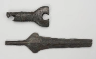 fragment miecza z brązu - Ujęcie z góry; Miecz z brązu zachowany we fragmencie - część głowni oraz rękojeść - o łącznej długości 22,7 cm. Egzemplarz cechuje smukła głownia, na powierzchni której przetrwała miejscami pierwotna lśniąca powłoka barwy ciemnozielonej. Dzięki temu widoczne są po obu stronach ostrza struziny podkreślone delikatnym zdobieniem w postaci drobnych nacięć i łuczków. Podobnym ornamentem, na który składają się pasma linii rytych i niewielkich nacięć, pokryta jest również rękojeść miecza o gładkiej ciemnozielonej powierzchni. Rękojeść jest niekompletna, brakuje jej głowicy – najpewniej tworzyły ją dwie niewielkie woluty, pomiędzy którymi wystawał niewielki pręt.