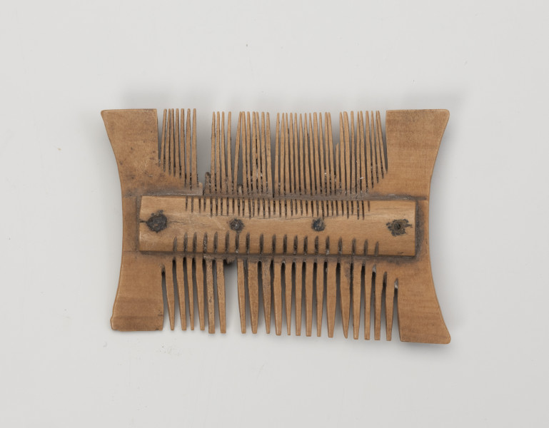 grzebień dwustronny grupa IIB, typ III - Ujęcie z przodu; Niewielki, dwustronny grzebień, wykonany z czterech płytek wyciętych z poroża, ułożonych obok siebie i przymocowanych do obustronnie występujących okładzin nitami wykonanymi ze stopu miedzi. Każdy nit znajduje się pośrodku jednej płytki. Po zmontowaniu konstrukcji wycinano za pomocą precyzyjnych piłek zęby, gęstsze u góry, z rzadziej rozmieszczona w dolnej cześci grzebienia. Powierzchnia została wygładzona, usunięto ślady obróbki surowca.