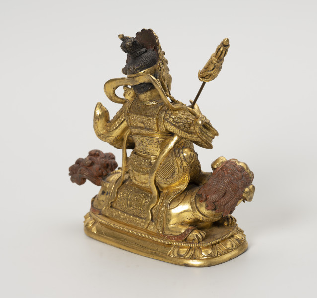 Wajśrawana (Dzambala) - ujęcie tyłu ze skosu z prawej; Złota, męska postać siedząca na złotym lwie. W prawej ręce trzyma chorągiew zwycięstwa (osobny, wyciągany element). Postać ma upięte w kok czarne włosy, szlachetnie ubrana: nosi diadem, liczne ozdoby z klejnotów, a jej strój przypomina zbroję wysokiej rangi dostojnika/króla. Lwa przedstawiono w pozycji wpółleżącej - waruje na ugiętych łapach. Obie postacie ustawiono na lotosowej podstawie. Posążek najprawdopodobniej przedstawia bóstwo bogactwa Wajśrawanę wraz z jego atrybutami.