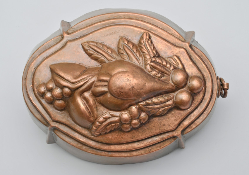 ujęcie z góry. Na wierzchu wytłoczona stylizowana gałązka z liśćmi i owocami: gruszką, orzechami, jagodami. Kolor miedziany.