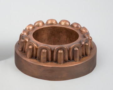 ujęcie 3/4. Niskie, walcowate naczynie. Nad wysokim cokołem cofnięty pas dekorowany powtarzającym się motywem wypukłego owalu, przypominającym kimation joński.