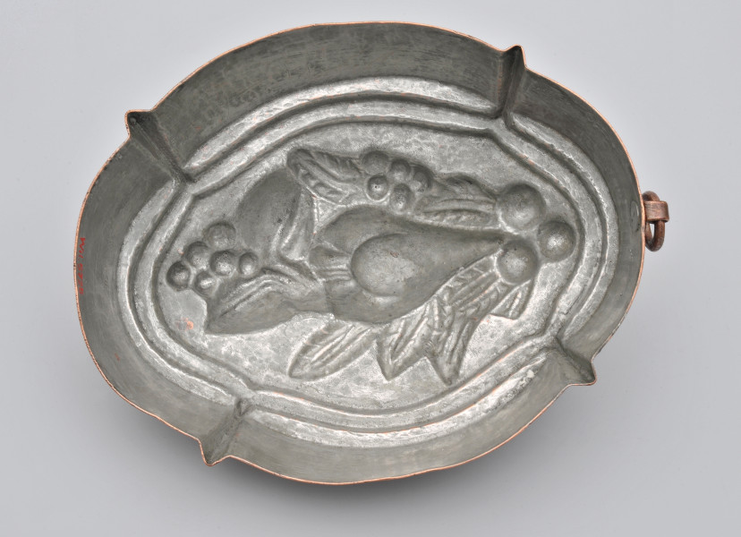 ujęcie z dołu. Naczynie o kształcie owalu z symetrycznymi czterema wypustkami na przekątnych. W polu środkowym wklęsła dekoracja z owocem gruszy. Kolor wnętrza srebrny.