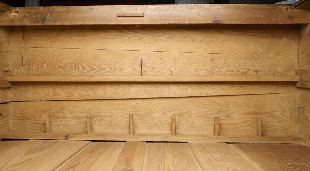 szafa - Szafa drewniana, dwudrzwiowa, w kolorze brązowym (kolor naturalnego drewna). Obiekt został z zewnątrz zabezpieczony lakierem. U dołu szafy widoczne dwie szuflady zamykane na klucz (brak kluczy; brak okucia zamka prawej szuflady). Wewnątrz, na tylnej ścianie, w jej górnej części umieszonych zostało siedem drewnianych wieszaków. W połowie wysokości zwieńczenia szafy widoczna pozioma listwa (ubytek listowy na prawej ścianie). Płyciny drzwi wykonane są z desek. Obiekt jest pozbawiony zdobień. Od spodu, w narożnikach szafy umieszczone zostały cztery podtrzymujące obiekt nogi wykonane z fragmentów deski i pomalowane żółto-brązową farbą olejną.W wnętrzu szafy, na tylnej ścianie oraz ścianach bocznych widoczne napisy oraz rysunki wykonane odręcznie ołówkiem. Na lewej ścianie widoczny napis: „Ta szafa była moi mieszkaniem ukrywalnym dn 21 II 43 r do dnia 25 IIII 43 r”, wizerunek nagiej kobiety stojącej bokiem i trzymającej ręce na kroczu (zasłaniającej się) oraz kobiety w kostiumie, której twarz jest ujęta z profilu, a jedna z nóg uniesiona do góry. Jej włosy są ułożone w fale. Pod nagą kobietą widniej podpis ,,(Głupia baba)’’. Nad kobietą w kostiumie napisano ,,(Francóska niewiasta)’’. Obok nagiej kobiety widoczna jest kolejna data: ,,20.1.43 r.’’.
Na tylnej ścianie widoczne są przedstawienia (od lewej strony): budynku mieszkalnego (domu jednorodzinnego),  wiatraka (pod nim), kobiety w spódnicy za kolano i kamizelce stojącej bokiem (obok, z prawej strony rysunku wiatraka), trzech postaci umieszczonych jedna pod drugą, niewielkiego samochodu (obok, z prawej strony postaci), drogowskazu (obok, z prawej strony samochodu), mężczyzny z długą brodą (Żyda; pod nim) ciągnącego za sobą konia oraz niedokończonej nagiej postaci przedstawionej tyłem (widoczne pośladki; pod rysunkiem konia).
Obok przedstawienia kobiety widoczny napis: ,,Hiszpańska dziewczyna’’. Pod spodem widoczny napis ,,Pffeferwehrtag | Przygody Tomcia | paluszki’’. Obok trzech postaci (ułożonych w linii jedna pod drugą) napis ,,(kąpiel)’’. Na drogowskazie napis ,,Do Palestyny 3814 km’’. Obok mężczyzny z brodą widoczny napis wersalikami „HIR, JUDE, DI, AŁH, JUDE’’.
Na prawej ścianie szafy widoczne przedstawienie zbliżenia cielesnego (dwóch nagich postaci połączonych ze sobą w uścisku), które zostało częściowo starte.
Wszystkie rysunki widoczne na ścianach bocznych zostały wykonane z boku zwrócone są górą do tylnej ściany obiektu. Rysunki widoczne na tylnej ścianie obiektu usytuowane są do góry nogami (odwrócone o 180° w stosunku do dna szafy).