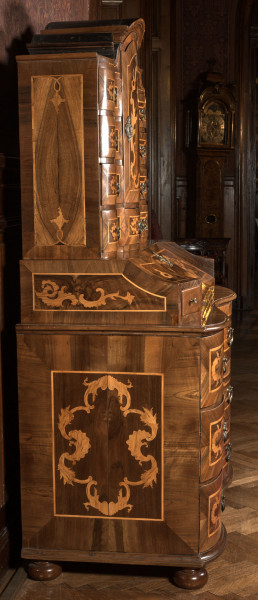 mebel o konstrukcji skrzyniowej, z wybrzuszonym frontem, na czterech kulistych nogach, wykonany z drewna iglastego, odłogowany (okleinowany) orzechem i intarsjowany jesionem (?) w motyw rocaili, część dolną mebla stanowi komoda o trzech szufladach; na niej sekretarzyk z uchylnym blatem-drzwiczkami ustawionym pod kątem i flankowanym dwiema szufladkami, wewnątrz dwa rzędy po cztery mniejsze szufladki; nastawa w formie szafki jednodrzwiowej z flankującymi ją szufladami (po cztery z każdej strony i pod drzwiczkami szafki