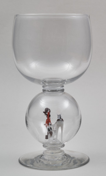 ﻿Kielich w typie „Römer”. Posiada półkolistą czaszę z cylindrycznym zwężeniem u góry. Charakterystyczny jest nodus w kształcie kuli. Kielich zakończony jest okrągłą, gładką stopą. Stopa i czara połączone są z nodusem pierścieniami. W nodus wtopiona jest scena myśliwska.