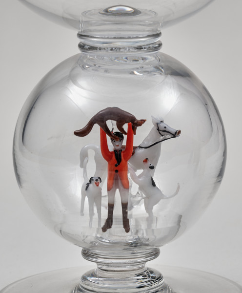 ﻿Kielich w typie „Römer”. Posiada półkolistą czaszę z cylindrycznym zwężeniem u góry. Charakterystyczny jest nodus w kształcie kuli. Kielich zakończony jest okrągłą, gładką stopą. Stopa i czara połączone są z nodusem pierścieniami. W nodus wtopiona jest scena myśliwska.