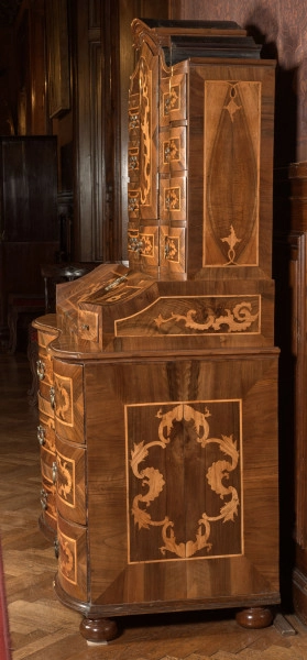 mebel o konstrukcji skrzyniowej, z wybrzuszonym frontem, na czterech kulistych nogach, wykonany z drewna iglastego, odłogowany (okleinowany) orzechem i intarsjowany jesionem (?) w motyw rocaili, część dolną mebla stanowi komoda o trzech szufladach; na niej sekretarzyk z uchylnym blatem-drzwiczkami ustawionym pod kątem i flankowanym dwiema szufladkami, wewnątrz dwa rzędy po cztery mniejsze szufladki; nastawa w formie szafki jednodrzwiowej z flankującymi ją szufladami (po cztery z każdej strony i pod drzwiczkami szafki