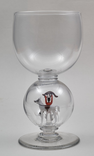 ﻿Kielich w typie „Römer”. Posiada półkolistą czaszę z cylindrycznym zwężeniem u góry. Charakterystyczny jest nodus w kształcie kuli. Kielich zakończony jest okrągłą, gładką stopą. Stopa i czara połączone są z nodusem pierścieniami. W nodus wtopiona jest scena myśliwska.