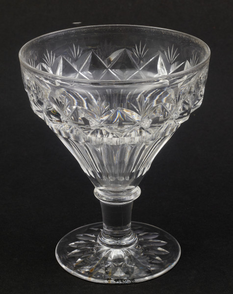 Stopa okrągła, nóżka krótka i szeroka, zakończona pierścieniem, na którym osadzona stożkowata czara. Spód stopy dekorowany płytkim szlifem o motywie wielopłatkowego kwiatka.