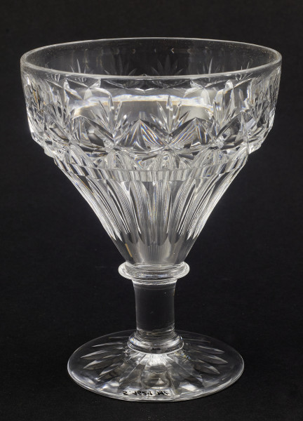 Kieliszek okrągły, ozdobiono szlifowaną dekoracją rośliną. Stopa okrągła, nóżka krótka i szeroka, zakończona pierścieniem, na którym osadzona stożkowata czara. Spód stopy dekorowany płytkim szlifem o motywie wielopłatkowego kwiatka.