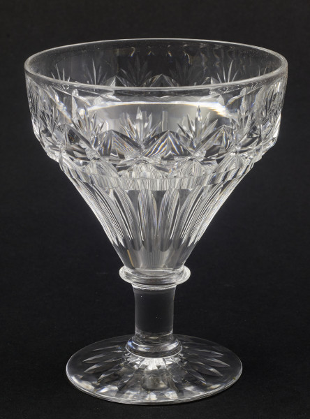 Kieliszek okrągły, ozdobiono szlifowaną dekoracją rośliną. Stopa okrągła, nóżka krótka i szeroka, zakończona pierścieniem, na którym osadzona stożkowata czara. Spód stopy dekorowany płytkim szlifem o motywie wielopłatkowego kwiatka.