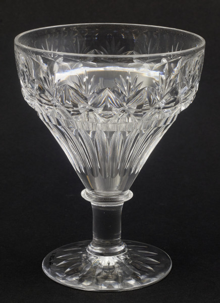 Kieliszek okrągły, ozdobiono szlifowaną dekoracją rośliną. Stopa okrągła, nóżka krótka i szeroka, zakończona pierścieniem, na którym osadzona stożkowata czara. Spód stopy dekorowany płytkim szlifem o motywie wielopłatkowego kwiatka.