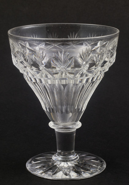 Kieliszek duży, wykonano ze szkła kryształowego
Stopa okrągła, nóżka krótka i szeroka, zakończona pierścieniem, na którym osadzona stożkowata czara. Spód stopy dekorowany płytkim szlifem o motywie wielopłatkowego kwiatka.
