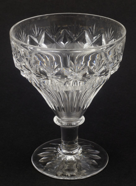 Kieliszek okrągły, ozdobiono szlifowaną dekoracją rośliną. Stopa okrągła, nóżka krótka i szeroka, zakończona pierścieniem, na którym osadzona stożkowata czara. Spód stopy dekorowany płytkim szlifem o motywie wielopłatkowego kwiatka.