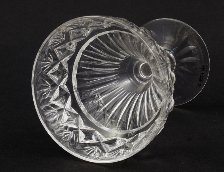 Kieliszek okrągły, ozdobiono szlifowaną dekoracją rośliną. Stopa okrągła, nóżka krótka i szeroka, zakończona pierścieniem, na którym osadzona stożkowata czara. Spód stopy dekorowany płytkim szlifem o motywie wielopłatkowego kwiatka.