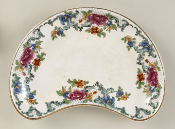 Płytki talerzyk o małych rozmiarach, wykonany z białego fajansu, służący do podawania przystawek obiadowych. Kształt naczynia nawiązuje do rynienki w formie nerki lub półksiężyca