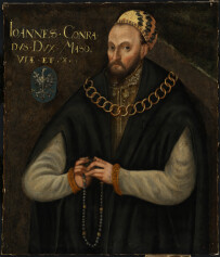 Portret Jana Konrada III Rudego, Konrad III Rudy (książę czerski 1471-1495; książę warszawski 1488-1495; książę Mazowsza 1495-1503) w ujęciu do pasa. Starszy, masywny mężczyzna w tradycyjnym stroju staropolskim. Ma piersi ma duży złoty łańcuch, w rękach, na wysokości brzucha trzyma różaniec, patrzy wprost na widza. Obraz utrzymany w zielonkawo-niebieskiej, zimnej tonacji. Fotografia gigapixel w bardzo wysokiej rozdzielczości.